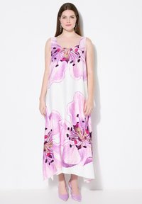 Ärmelloses Maxikleid in Weiß mit großem rosa Blumenmuster. Glattes Gewebe, A-Linie-Silhouette und ein hoher niedriger Saum. Kombiniert mit rosa Absätzen.