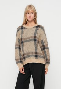 Beige geruite trui met bruine en marineblauwe lijnen, geribbelde ronde halslijn, lange mouwen en een relaxte pasvorm. Zachte, donzige textuur.