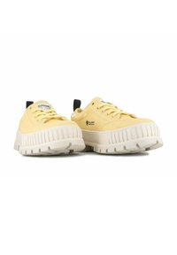 Zapatillas de lona amarillas con una gruesa suela de goma blanca, que presentan un diseño texturizado y una lengüeta negra en el talón.