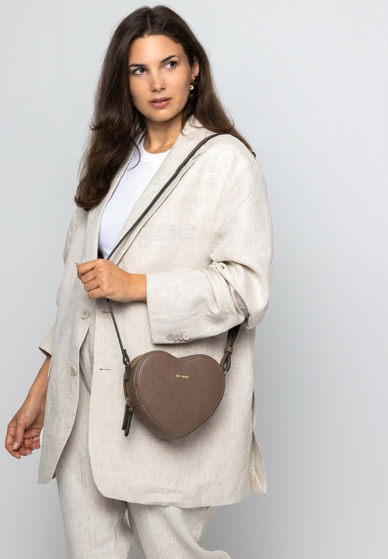 Braune herzförmige Handtasche aus strukturiertem Leder, mit abnehmbarem Schulterriemen und goldfarbenem Logo-Detail auf der Vorderseite.