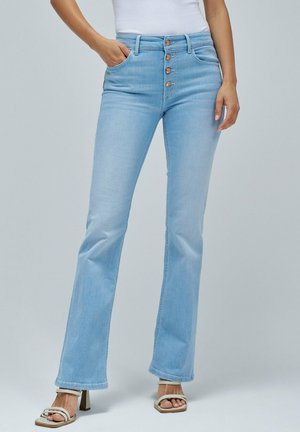 Light blue flared jeans with a high waist, five-button closure, and subtle shine, paired with light-colored strappy sandals.