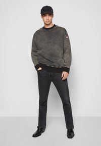 Gray sweatshirt with textured finish, black ribbed cuffs and hem, paired with dark jeans and black ankle boots, standing against a neutral background.