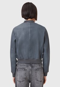 Giacca bomber in pelle grigia con polsini e orlo a costine, caratterizzata da una superficie liscia e un design semplice e minimalista.