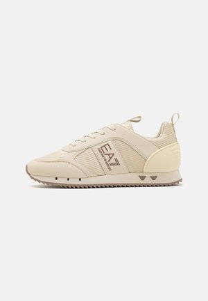 Baskets de sport beige en tissu en maille avec des accents lisses, dotées d'une semelle en caoutchouc avec un motif en zigzag et un détail de marque sur le côté.