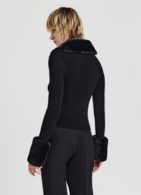 Schwarzer gerippter Pullover mit einem plüschigen Kunstfellkragen und -bündchen. Figurnahes Design mit langen Ärmeln, kombiniert mit eleganten schwarzen Hosen.