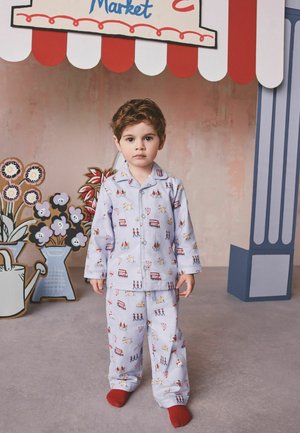 Junges Kind in hellblauer Schlafanzug mit London-Motiven steht barfuß auf einem grauen Boden unter einem rot-weiß gestreiften Marktzelt.