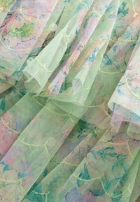 Áttetsző pasztell zöld anyag virágmintákkal, fodros rétegekkel és varrott részletekkel, amelyek texturált, finom megjelenést kölcsönöznek.