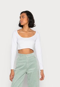 Top branco cropped de mangas compridas combinado com calças de tergal verde claro de cintura alta, apresentando uma textura suave e um corte reto.
