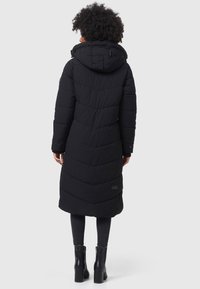 Svart puffjacka med huva, med chevron-söm, långa ärmar och sidfickor, kombinerad med svarta högklackade stövlar.