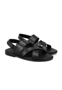 Schwarze Ledersandalen mit überkreuzten Riemen, flacher Sohle, offenes Fersen-Design und glatter Textur. Einfacher, minimalistischer Stil ohne zusätzliche Akzente.