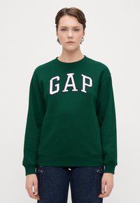 Grønn genser med ribbestrikkede mansjetter og nederkant, med fremtredende hvit "GAP" bokstaver i et kollegialt stil over brystet.