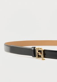 Μαύρη δερμάτινη ζώνη με λεία υφή, που διαθέτει αγκράφα από χρυσό μέταλλο με σχεδιασμό αλληλοσυνδεόμενων στοιχείων. Η εσωτερική πλευρά είναι μπεζ.