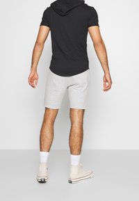 Černá mikina s krátkým rukávem a zakřiveným lemem, kombinovaná se světle šedými bavlněnými kraťasy. Nosená s bílými ponožkami a krémovými vysokými teniskami.