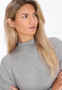 Hellgrauer Pullover mit hohem Kragen und langen Ärmeln, aus weichem, strukturiertem Stoff gefertigt. Verfügt über subtile Details am Halsausschnitt.
