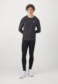 Černé atletické tričko s dlouhým rukávem s šedými detaily, doplněné o přiléhavé černé legíny a bílé tenisky, s atletickým střihem.