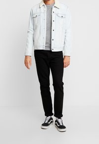 Hellblaues Denim-Jackett mit einem weißen Sherpa-Kragen, grauem Hemd, schwarzen Jeans und schwarzen Sneakers mit weißen Akzenten. Lässiges Outfit.