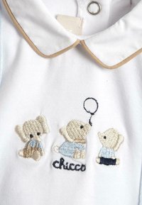 Witte katoenen kleding met een kraag met beige bies, drie geborduurde teddyberen in pastelkleuren en de tekst "chicco" eronder.