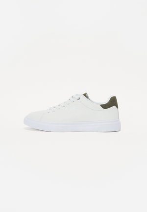 White sneaker with a smooth suede upper, contrasting olive green heel tab, round white laces, and a rubber sole. Minimalist design.