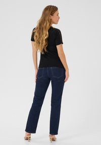 T-shirt noir avec des détails en dentelle sur les épaules, associé à un jeans denim bleu foncé, présentant une coupe droite et une broderie minimale sur les poches arrière.