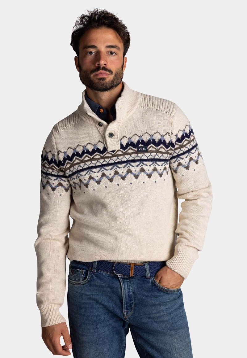 Crème-kleurige pullover trui met een hoge kraag, voorzien van een geometrisch patroon in blauw en bruin over de borst. Zachte gebreide textuur.