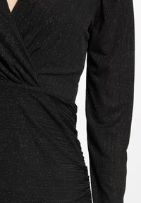 Robe noire à manches longues, avec un design enveloppant, un tissu texturé avec des paillettes métalliques et des détails froncés à la taille.