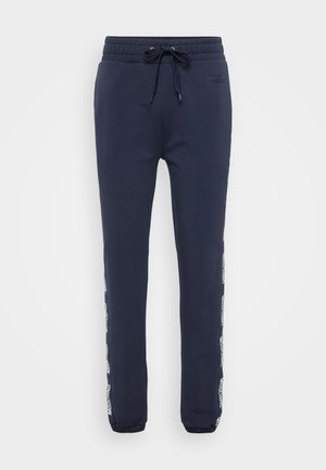 Pantalons de survêtement bleu marine avec taille élastique et cordon de serrage, poignets élastiques, et bandeau avec logo "Moschino" en blanc courant le long des côtés extérieurs.