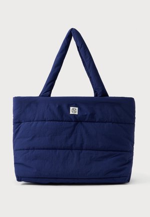 Marineblauwe doorgestikte tote tas met gewatteerde handvatten en een klein wit logopatch centraal vlak bij de bovenkant.