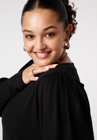 Zwarte trui met pofmouwen, zachte textuur, gedragen door een persoon. Gouden hoepelringen en een delicate ring zijn zichtbaar op de hand.