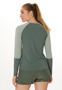 Langärmliges Hemd in Waldgrün mit hellgrünen Ärmeln, ausgestattet mit einer glatten Textur und Raglan-Design. Kombiniert mit grünen Shorts.