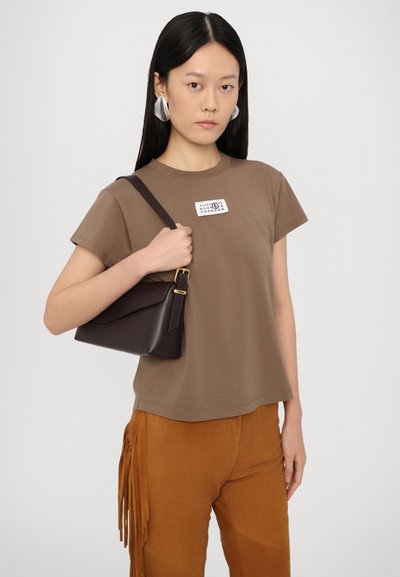 Bruine katoenen t-shirt met korte mouwen en een etikettering, gecombineerd met bruine suède broek met franjes en een kleine donkerbruine handtas.