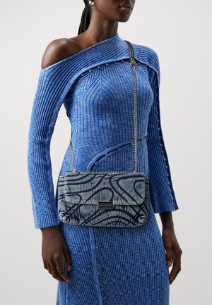 Blå ribbad klänning med off-shoulder-design. Modellen håller en blå mönstrad väska med ett metalliskt kedjerygg och en rektangulär lås.