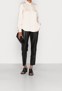 Chemise en satin rose clair à boutons avec un col, associée à un pantalon en cuir noir ajusté. Des mules à bout ouvert noires complètent le look.