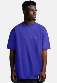 Oversized paarse T-shirt met korte mouwen, voorzien van een wit geborduurd logo op de borst en een gladde, licht gestructureerde stof.