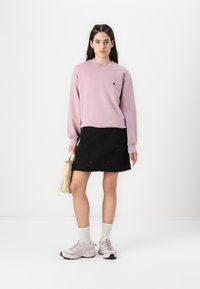 Ljusrosa sweatshirt med en liten logotyp, svart kjol, beige handväska och ljusrosa sneakers med grå accenter samt strumpor i ankellängd.