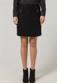 Svart kjol i ett slätt tyg med två framfickor med dragkedja och en figurnära design. Matchad med svarta ankelstövlar.