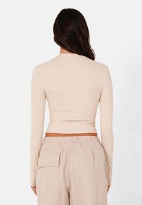 Beige lange mouwen top met een aansluitend ontwerp en hoge hals. Gepaarde met losse beige broek met zijs pockets en een elastische tailleband.