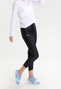 Černé sportovní legíny, přiléhavý střih, spárované s bílým topem s dlouhým rukávem a světle modrými běžeckými botami s síťovými akcenty.