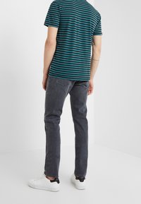 Camisa a rayas en tonos verde azulado y navy de manga corta, combinada con un pantalón oscuro gris y zapatillas blancas con un acento negro en el talón.