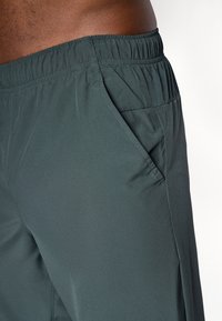 Mørkegrå, vide bukser i let materiale med elastisk talje og en sidelomme. Stoffet har en glat overflade og en afslappet pasform.