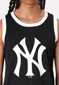 Juodas be rankovių džersis su baltais akcentais ir dideliu baltu Niujorko "Yankees" logotipu. Pagamintas iš lygios medžiagos, turi apvalią kaklą.