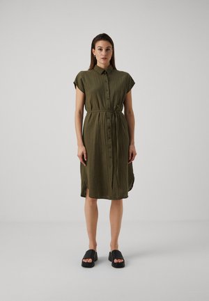 Olive green, button-up dress with short sleeves and a belted waist. Features a textured fabric and side slits. Worn with black platform sandals.