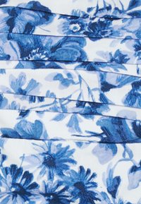 Blauw-witte bloemenstof met geplooide lagen, featuring verschillende bloemvormen en bladvormen.