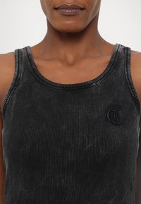 Svart ribbet tanktopp med rund halslinning, teksturert stoff og brodert logo på brystet.