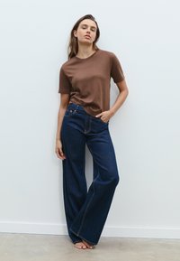 Brun kortärmad t-shirt i kombination med mörkblå vid jeans med vida ben. Jeansen har framfickor och kontrasterande sömmar.