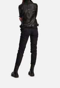 Schwarze Lederjacke mit hohem Kragen; taillierter Schnitt. Schwarze Jeans mit schmalem Bein und Gesäßtaschen. Schwarze Knöchelstiefel mit kräftigen Sohlen.