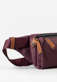 Marsupio bordeaux realizzato in tessuto resistente, dotato di una cerniera nera con tiranti in pelle marrone e una tracolla regolabile per un indosso sicuro.