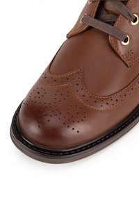 Hnedá kožená topánka s okrúhlou špičkou, brogue detailmi, hnedými šnúrkami a zlatými očkami, s kontrastným prešívaním a hladkým povrchom.