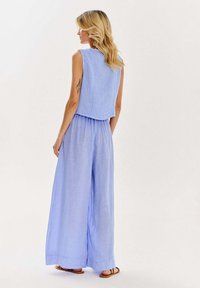 Svetlo modrá bezrukávová blúzka v kombinácii s širokými nohavicami, obe vyrobené z mäkkej, textúrovanej látky. Nohavice majú zbaliteľný pás a ohybné manžety.