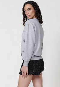 Felpa grigia con embellishments testurizzati, polsini a costine e una vestibilità comoda, abbinata a pantaloni corti in tweed neri con orlo frangiato.