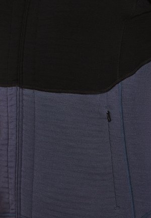 Color-blocked athletic top with black upper section and dark blue lower section. Features textured fabric and a side zipper pocket.